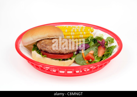 Türkei Burger mit Salat und Tomaten in Brötchen in rot Retro Kunststoffkorb mit Ohr von Mais und Salat auf weißem Hintergrund Ausschnitt. Stockfoto