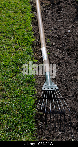 Holzgriff behandelt Rake auf frischen frisch gedrehten Boden neben fein säuberlich geschnittenen abgeschnittenen grünen Rasen Stockfoto