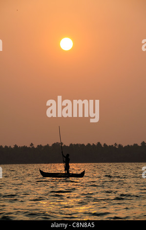 Vertikale Schuss des Sonnenuntergangs am Vembanad See, Kerala, Indien, mit Fährmann Stechkahn fahren seine Holzboot über den See im Vordergrund Stockfoto