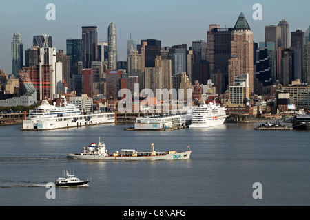 Boote auf dem Hudson River, die an angedockten Kreuzfahrtschiffen vorbeifahren. Das Boot in der Mitte des Flusses ist ein Schlammboot. Stockfoto