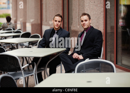 Weiten Blick über zwei scharfe angezogene junge Geschäftsleute in einem Straßencafé in einer Innenstadt und Umgebung. Stockfoto