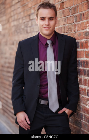 Hübscher junger Geschäftsmann tragen Anzug und Krawatte, eine rote Mauer gelehnt. Stockfoto