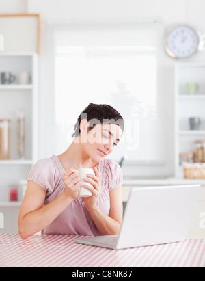Lächelnde Frau hält eine Tasse mit einem Laptop arbeiten Stockfoto
