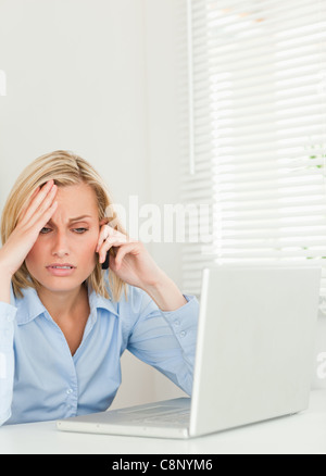 Frustriert blonde Geschäftsfrau sitzen vor ihrem Notebook auf Handy Stockfoto