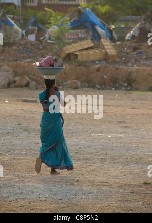 Eine junge Frau geht durch die Schmutz-Feld auf dem Weg zu dem Slum, die Güter auf dem Kopf gegenüber dem Bus Pick up Punkt Stockfoto