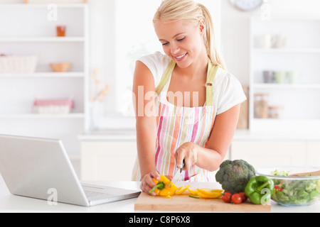 Nahaufnahme von einer blonden Frau mit einem Notebook eine Paprika schneiden Stockfoto