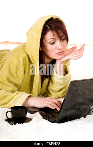 Frau in Robe mit Laptop auf dem Boden liegend Stockfoto