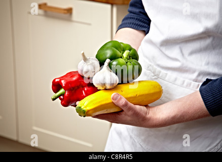 Koch hält verschiedene Gemüse in Hände inmitten der modernen Küche. Chef trägt weißen Schürze. Stockfoto