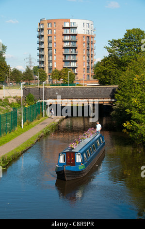 Ein Schmalboot auf dem Ashton Canal, Clayton, Eastlands, Manchester, England, Großbritannien. Der Drum Appartementblock dahinter. Stockfoto