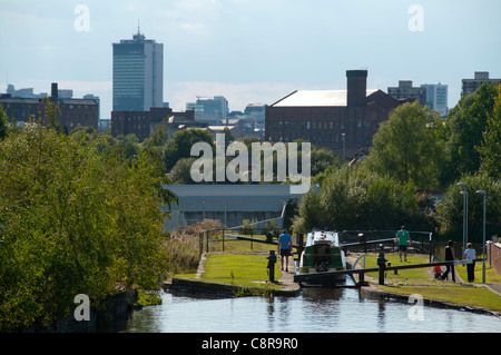 Ein Narrowboat in eine Sperre für Ashton Canal, Clayton, Eastlands, Manchester, England, UK.  Stadtturm (Piccadilly Plaza) hinter. Stockfoto