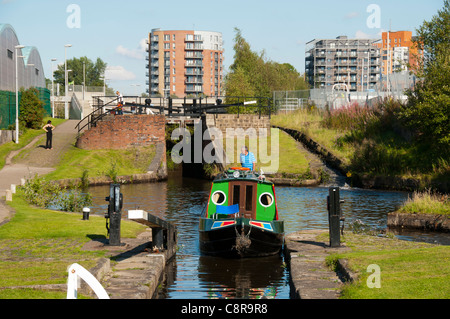 Ein Schmalboot, das in eine Schleuse auf dem Ashton Canal, Clayton, Eastlands, Manchester, England, Großbritannien, einfährt. Der Drum Appartementblock dahinter. Stockfoto