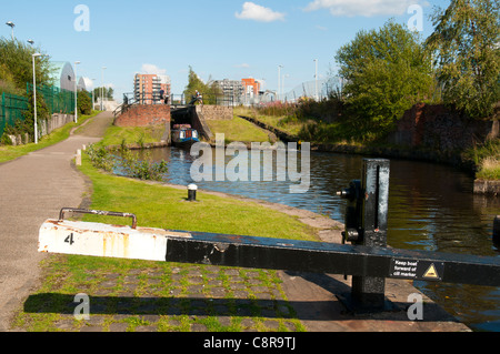 Ein Schmalboot, das aus einer Schleuse auf dem Ashton Canal, Clayton, Eastlands, Manchester, England, Großbritannien, fährt. Der Drum Appartementblock dahinter. Stockfoto