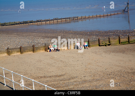 Leute sitzen am Sandstrand von hölzernen Buhnen, Hornsea, Yorkshire, England Stockfoto