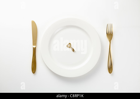 Goldener Schlüssel auf Teller mit Messer und Gabel neben Stockfoto