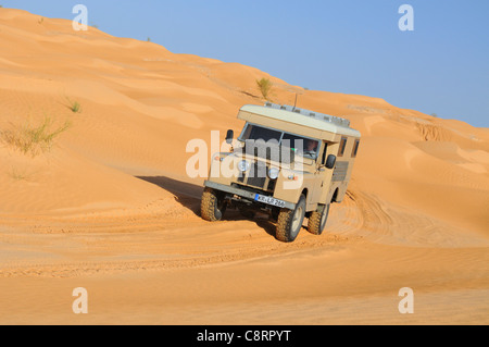 Afrika, Tunesien, nr. Tembaine. Wüste Reisende fahren eine Ex-Armee 1966 Land Rover Serie 2a Krankenwagen durch einen Sandfield... Stockfoto