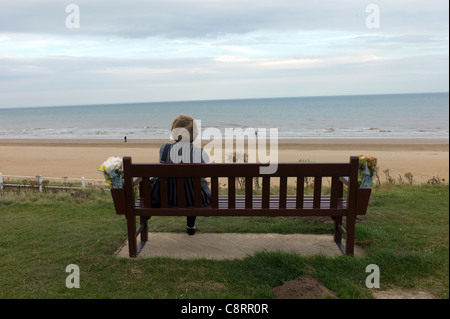 Frau saß auf einem Denkmal Bank mit Blick auf South Bay Strand in Bridlington, Yorkshire, Großbritannien Stockfoto