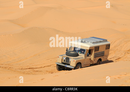 Afrika, Tunesien, nr. Tembaine. Wüste Reisende fahren eine Ex-Armee 1966 Land Rover Serie 2a Krankenwagen durch einen Sandfield... Stockfoto