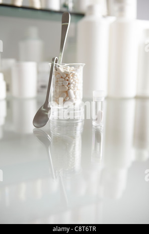 Becher gefüllt mit Pillen und Kapseln mit Tablettenfläschchen im Hintergrund Stockfoto