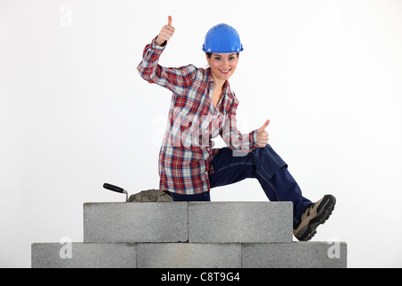 Frau Maurer sitzen auf einer Mauer machen Daumen hoch Zeichen Stockfoto