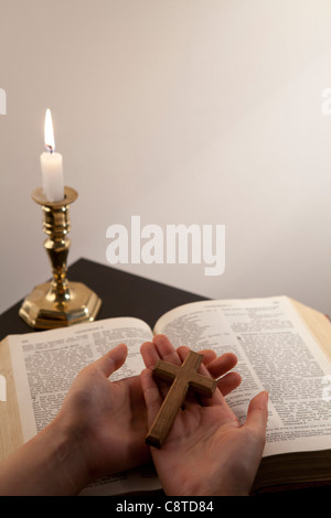 Hände halten hohen Winkel Kreuz mit Bibel und Kerze im Hintergrund Stockfoto