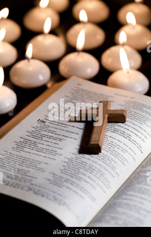 Kreuz auf Bibel liegend mit Kerzen im Hintergrund Stockfoto