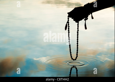 Hand, die indischen Rudraksha / Japa Mala Gebet Perlen über Plätschern des Wassers. Silhouette Stockfoto