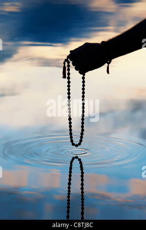 Hand, die indischen Rudraksha / Japa Mala Gebet Perlen über Plätschern des Wassers. Silhouette