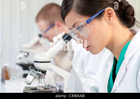 Eine chinesische asiatische medizinische oder wissenschaftliche Forscherin oder Arzt unter dem Mikroskop im Labor mit ihrer Kollegin Stockfoto