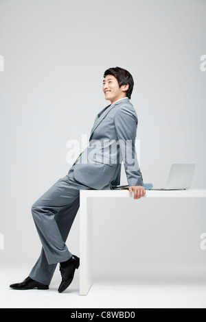 Portrait Of Smiling asiatischen Geschäftsmann stützte sich auf Schreibtisch, Laptop und Datei auf Schreibtisch Stockfoto