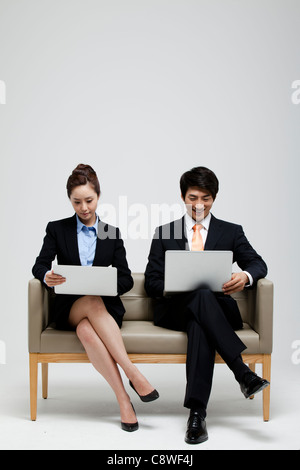 Asiatische Geschäftsfrau und Geschäftsmann auf Sofa mit Laptop Stockfoto