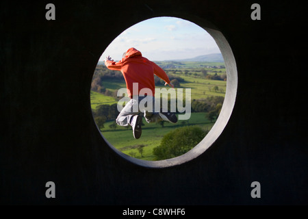 Kinder im Spiel   junge springen aus dem "Atom"  Pendle Panoptikum, Wycoller Country Park, Lancashire, UK Stockfoto