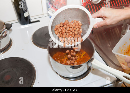 Frau Bohnen aus einem Sieb in einen Topf gießen Stockfoto