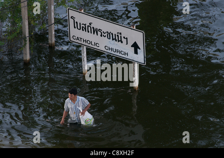 Thai Mann watet, überschwemmten Autobahn Vergangenheit eine zweisprachige direktionale Zeichen in Rangsit, einem nördlichen Vorort von Bangkok, Thailand. Mittwoch, November 2nd, 2011. Thailand erlebt die schlimmste Überschwemmung in mehr als 50 Jahren. Quelle: Kraig Lieb Stockfoto