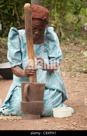 Eine Frau Pfund Erdnüsse mit einem Mörser und Stößel vor ihrem Haus in Kibuku District, Uganda. Stockfoto