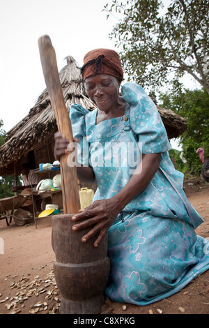 Eine Frau Pfund Erdnüsse mit einem Mörser und Stößel vor ihrem Haus in Kibuku District, Uganda. Stockfoto