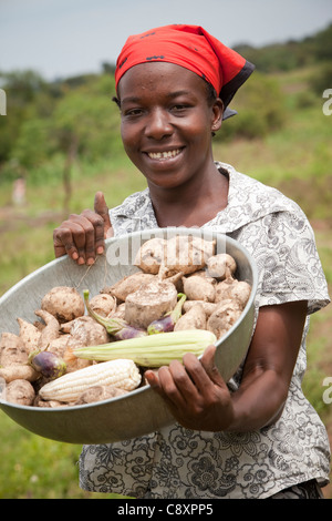 Eine junge Frau zeigt eine Ernte von Süßkartoffeln und Gemüse aus dem Garten der Familie in Kibuku District, Uganda. Stockfoto