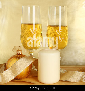 Zwei Gläser Champagner, Goldband und Weihnachtskugel mit einer brennenden Kerze auf einem goldenen Hintergrund Stockfoto