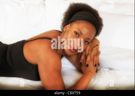 Attraktive schwarze Frau afroamerikanischen Seitenansicht liegen auf weißer Bettwäsche tragen schwarzes Lycra-Oberteil stützte sich auf Ellenbogen-Diamant-band Stockfoto