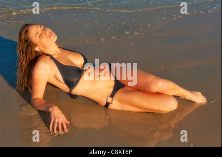 Schöne junge Frau entspannt 20-24 auf nassen Sand am Strand Kopf Gesichter Sonne liegend, am späten Nachmittag Stockfoto