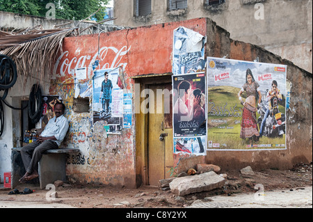 Indien Mann draußen ein tattered Wand eines alten ländlichen indischen Haus in indischen Film Poster abgedeckt. Puttaparthi, Andhra Pradesh, Indien Stockfoto