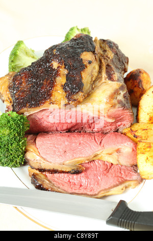 Eine geröstete Fuge von Balsamico glasiert Rindfleisch Lende auf einem Teller mit Bratkartoffeln und gekochten Brokkoli und einem Schnitzmesser, vertikale Stockfoto