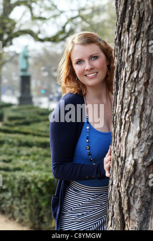 lächelnde junge Frau hinter Baum Stockfoto