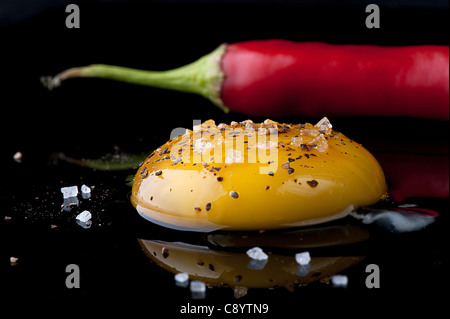 Rohes Ei mit Salz und Pfeffer und roten Paprika auf einem schwarzen reflektierenden Oberfläche. Stockfoto