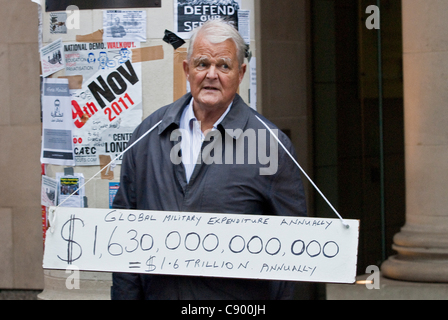 Bruce Kent, ein britischer politischer Aktivist und ehemaliger katholischer Priester, mit einem Schild anzeigen grauenhaft Menge der weltweiten militärischen Ausgaben jährlich, St Pauls LSX Protestdemonstration, London, 5. November 2011 Stockfoto