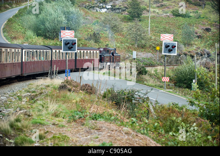 2 ft. Schmalspur Dampf Lok double Fairlie "Merddin Emrys" zieht seinen Zug über einen Bahnübergang über eine Straße auf dem Weg zu Porthmadog auf die wieder-Bahn verläuft zwischen Porthmadog und Blaenau Ffestiniog, Snowdonia, North Wales, UK. Stockfoto