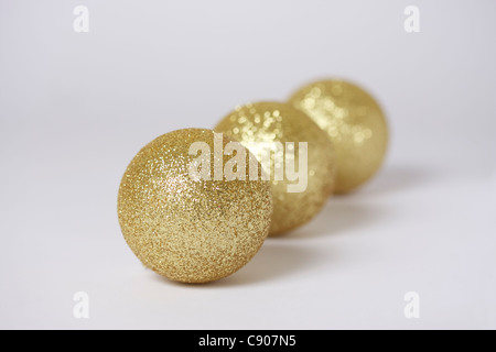 Drei gold farbigen Weihnachtsschmuck in Diagonale Linie von links nach rechts angeordnet. Weißer Hintergrund, Fokus auf vorderen Christbaumkugel. Stockfoto