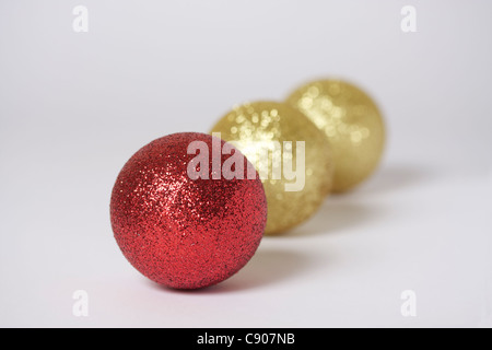 Drei 3-Weihnachtsschmuck mit Fokus auf Vorderseite der Rote Christbaumkugel mit zwei gold farbigen Kugeln verschwommen im Hintergrund angeordnet. Stockfoto