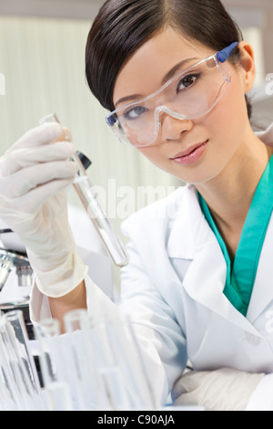 Eine chinesische asiatische medizinische oder wissenschaftliche Forscherin oder Arzt mit Blick auf ein Reagenzglas klare Flüssigkeit in einem Labor Stockfoto