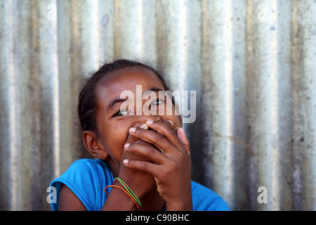 Ein schüchternes junges Mädchen mit dunklen schwarzen Augen Lächeln auf den Lippen, aber ihr Lächeln mit ihren Händen in Hell-Ville, Nosy Be, Madagaskar versteckt Stockfoto