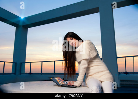 Attraktive junge Hispanic Frau der 20er Jahre entspannt auf Dachterrasse Wohnhaus und befasst sich mit Fotos von sich auf computer Stockfoto